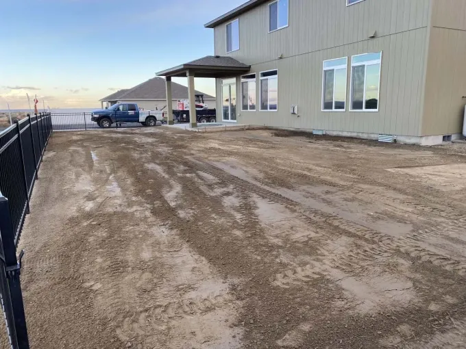 Mud-covered driveway beside a beige metal building, with a car and covered entrance under a cloudy sky.