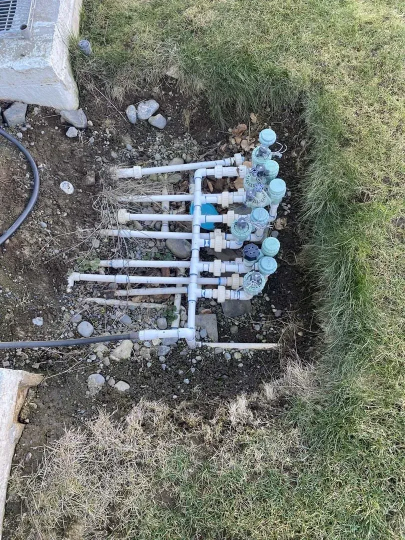 White PVC pipes with blue valve caps laid in a grassy trench beside concrete edging.