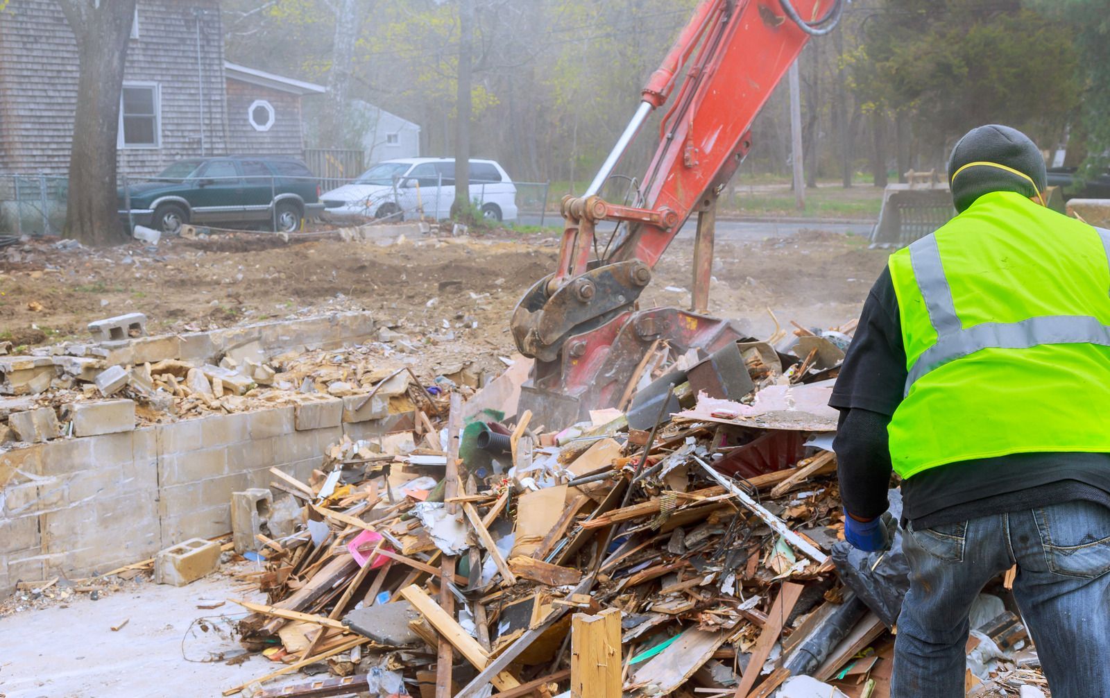 Worker in neon safety vest operating excavator to clear debris at a demolition site.