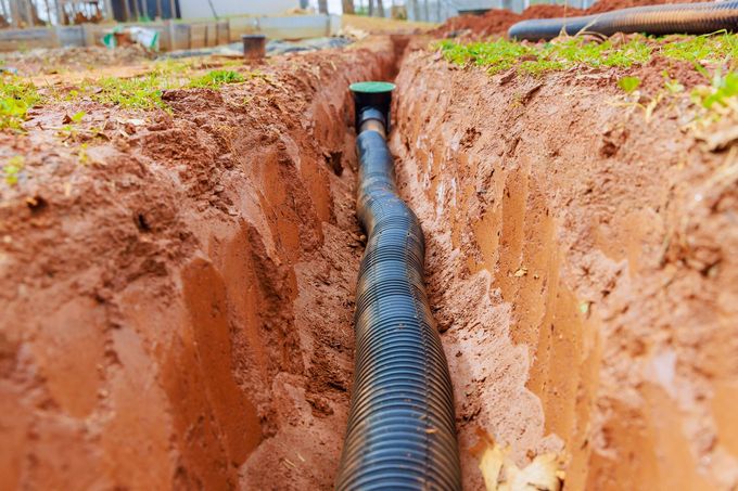 Black corrugated pipe laid in a narrow trench of reddish soil at a construction site