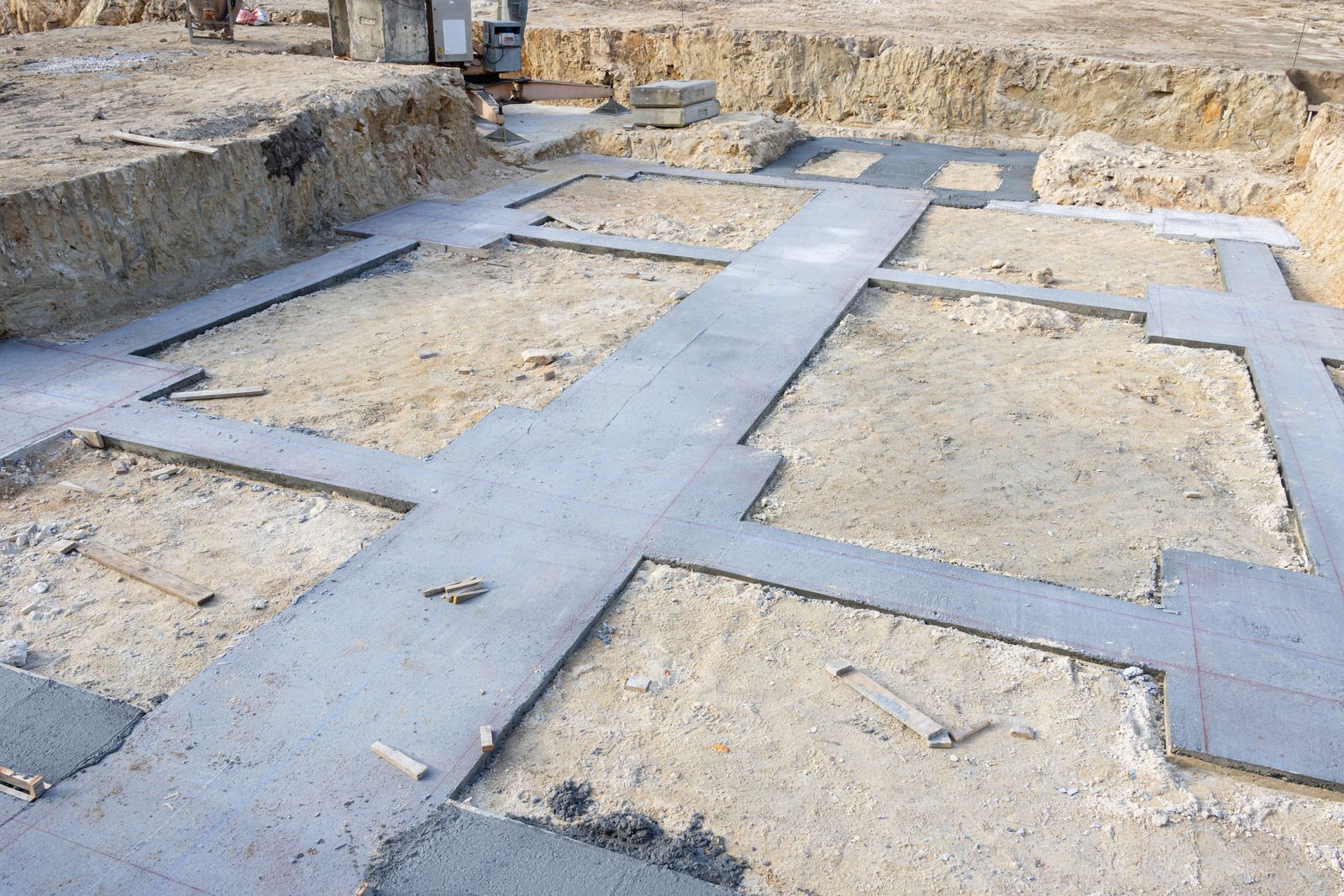 Excavated foundation with blue-gray concrete strip footings forming a grid in sandy soil