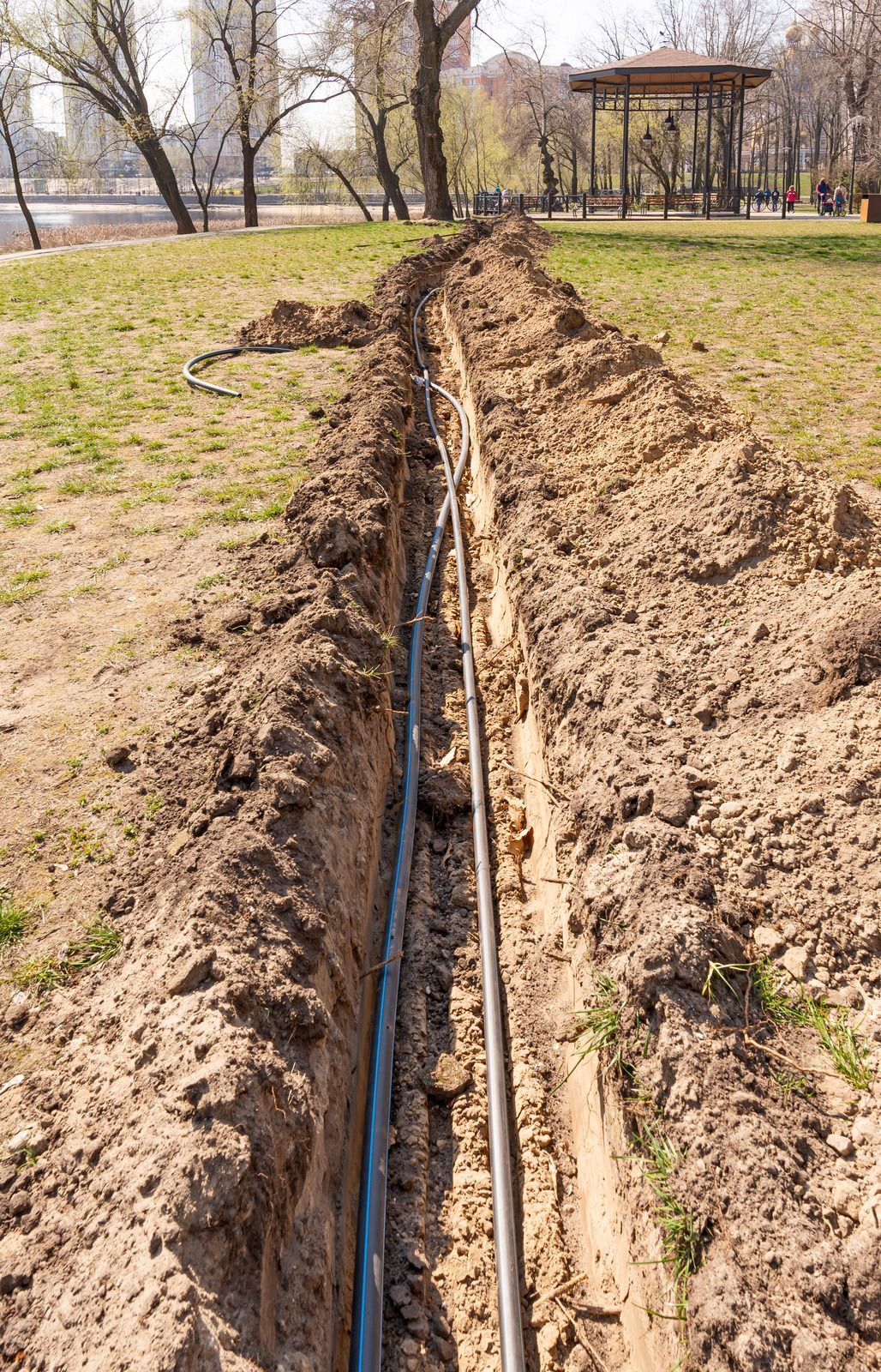 Trench in a grassy park with a black cable running down the center.