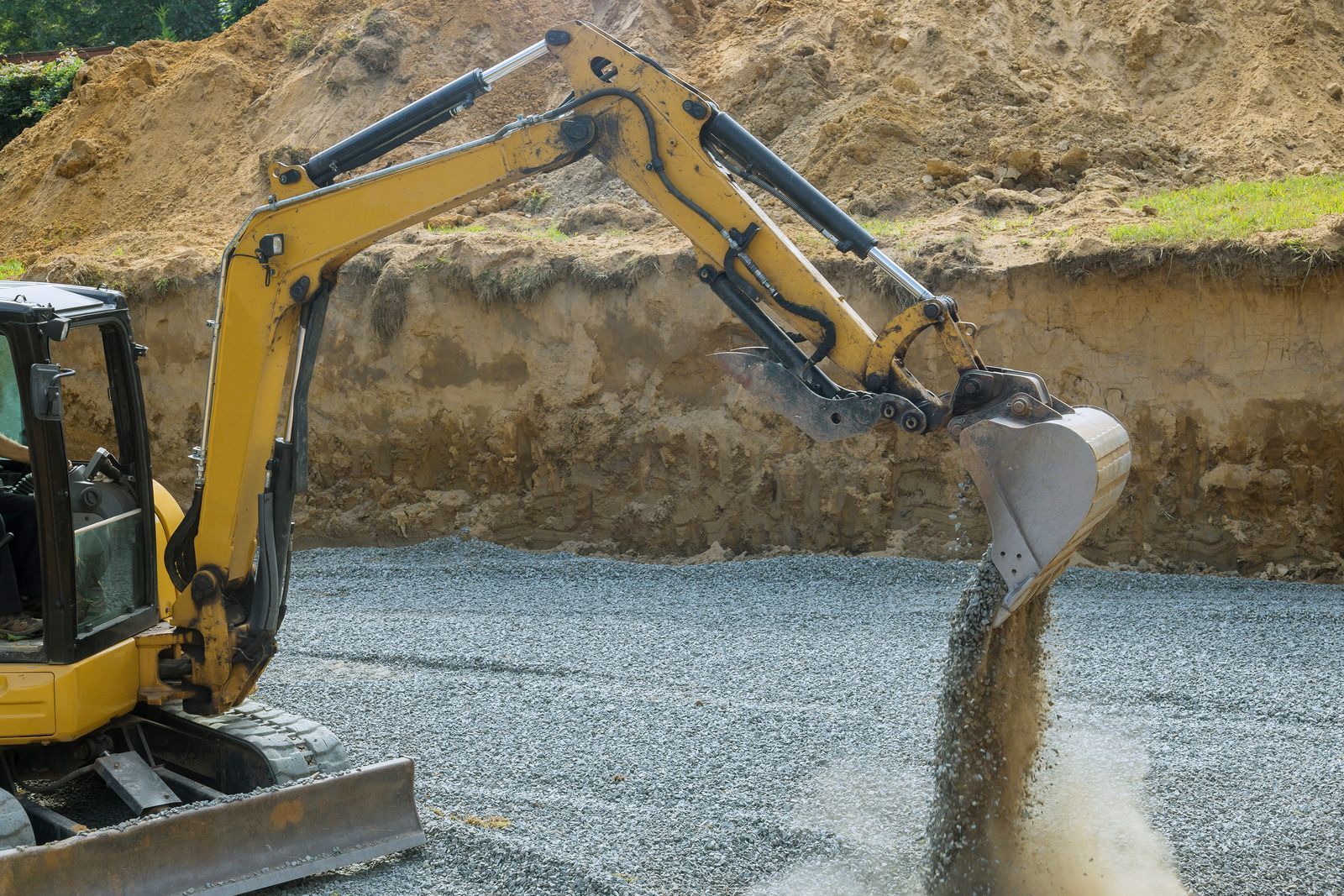 Excavator dumping gravel into a trench at a construction site