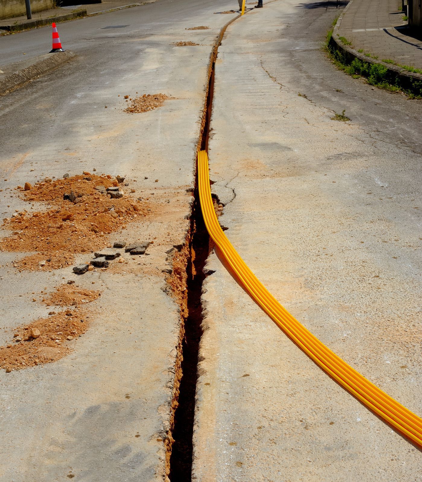 Orange cable lying in a cracked road trench on a curved street, with dirt scattered nearby.