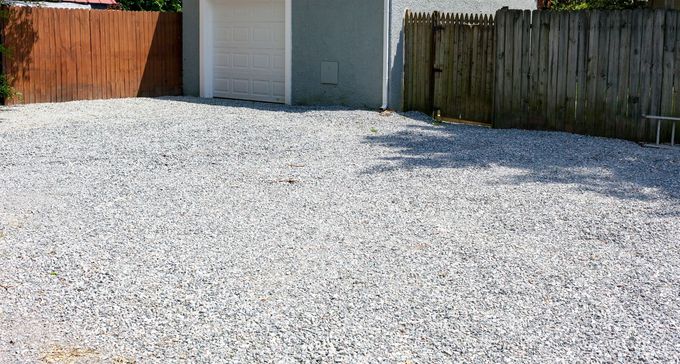 Gravel driveway leading to a white garage, bordered by wooden fences on both sides.