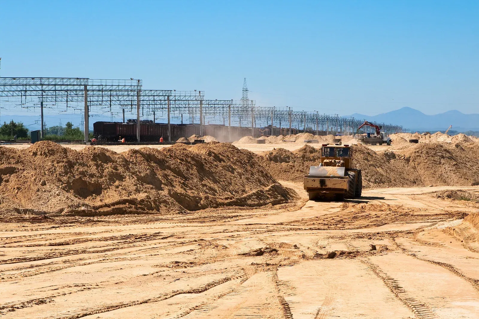 Bulldozer grading a sandy construction site with power lines and mountains in the background