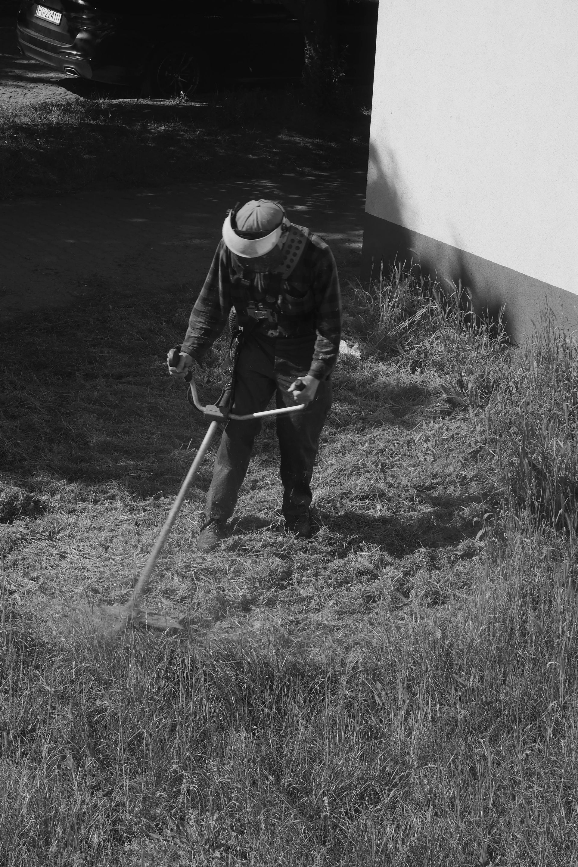 Person using a weed wacker to cut tall grass near a building.