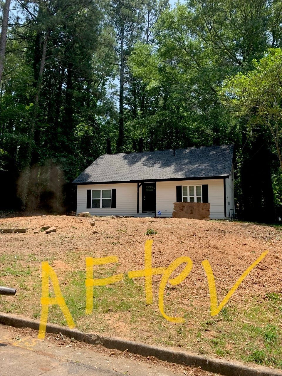 A small white house with a black roof, surrounded by trees. The front yard is dirt, and it has “AFTER” written on it.
