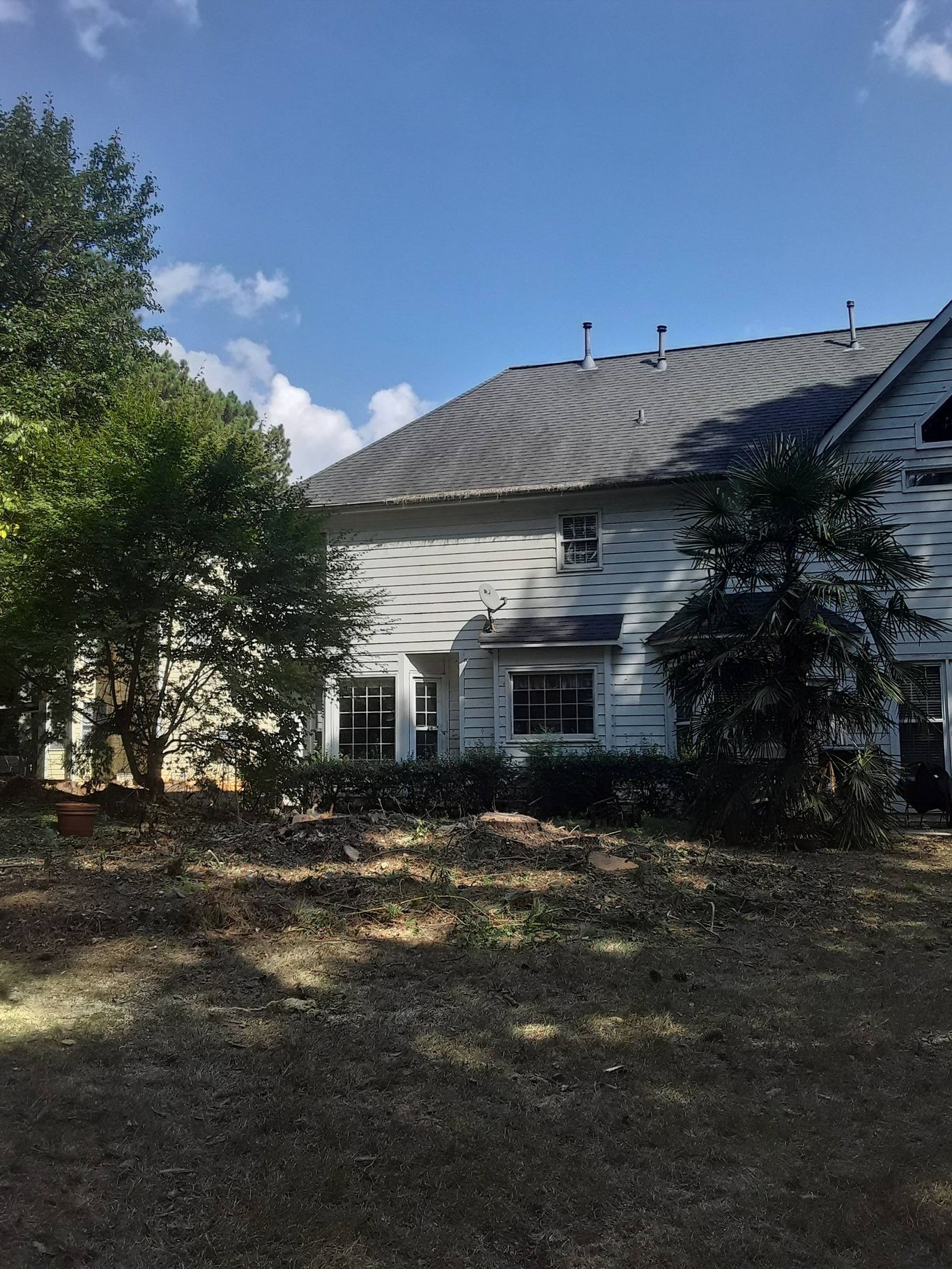 Side view of a two-story white house with a dark gray roof, surrounded by trees and a brown yard.