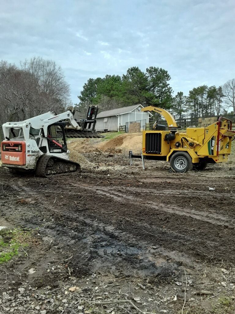 Bobcat skid steer and wood chipper on muddy ground near a house.