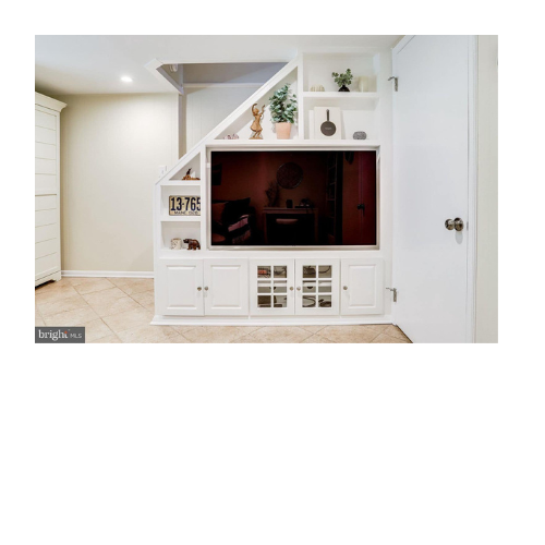 A living room with a tv on a shelf under a staircase.