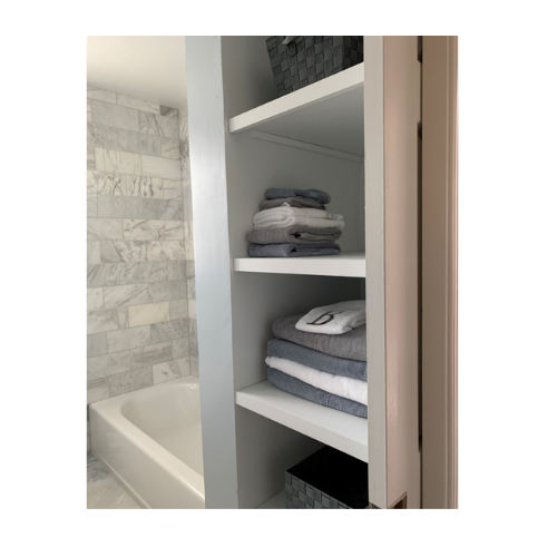A bathroom with a bathtub and shelves filled with towels.