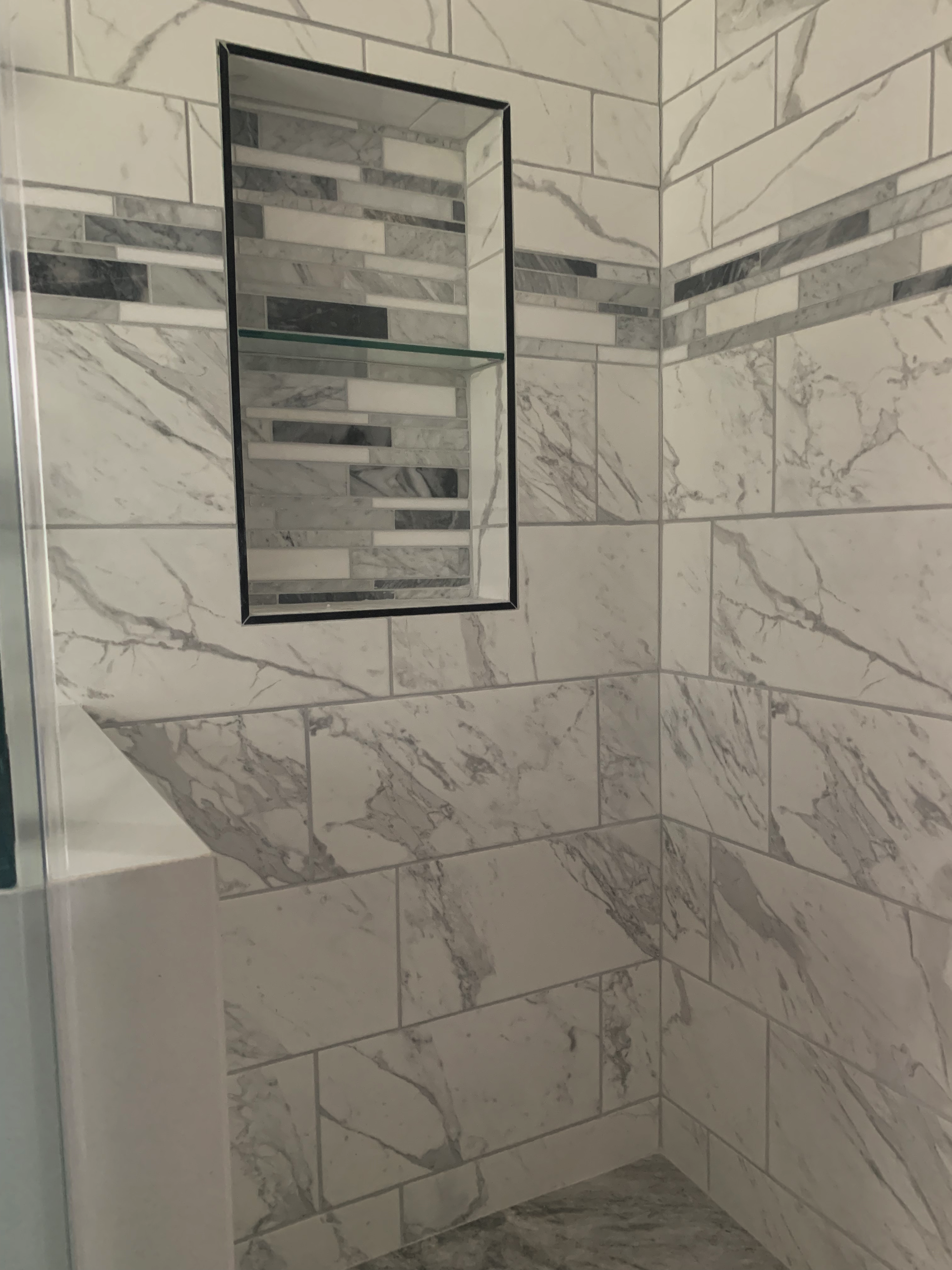 A shower with marble tiles and a mirror on the wall.