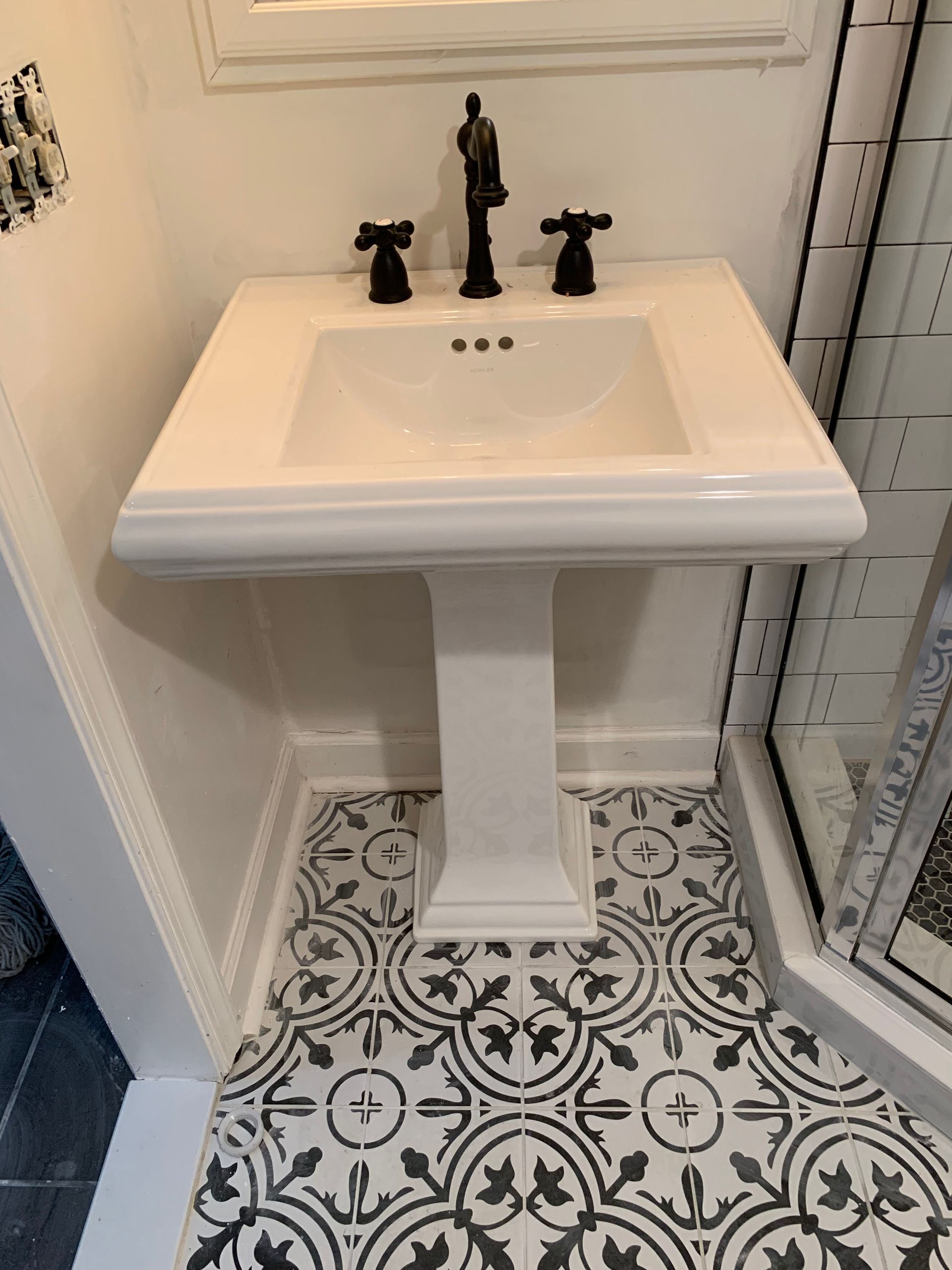 A bathroom with a pedestal sink and a black and white tile floor.