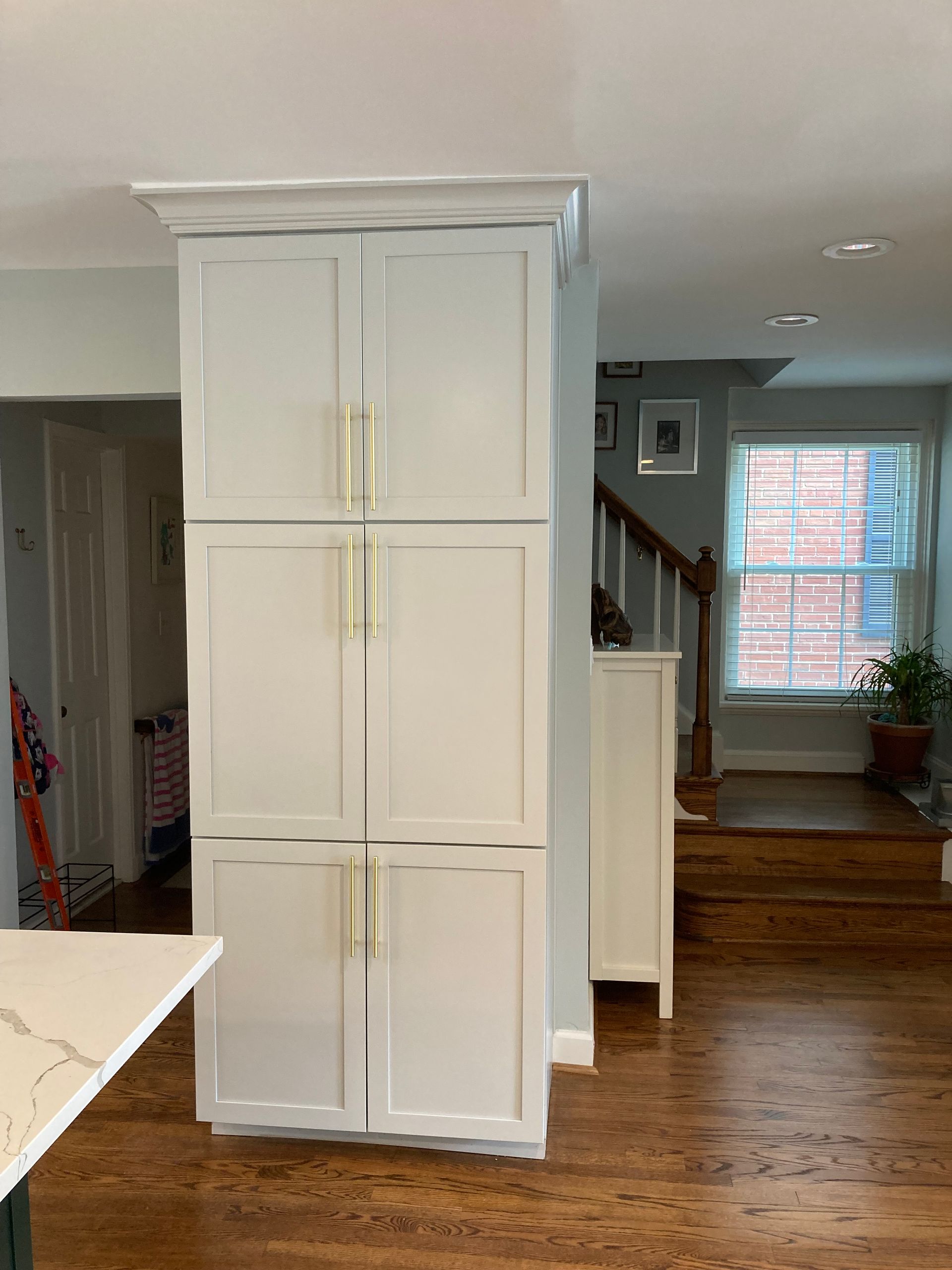 A kitchen with white cabinets and hardwood floors and a staircase in the background.