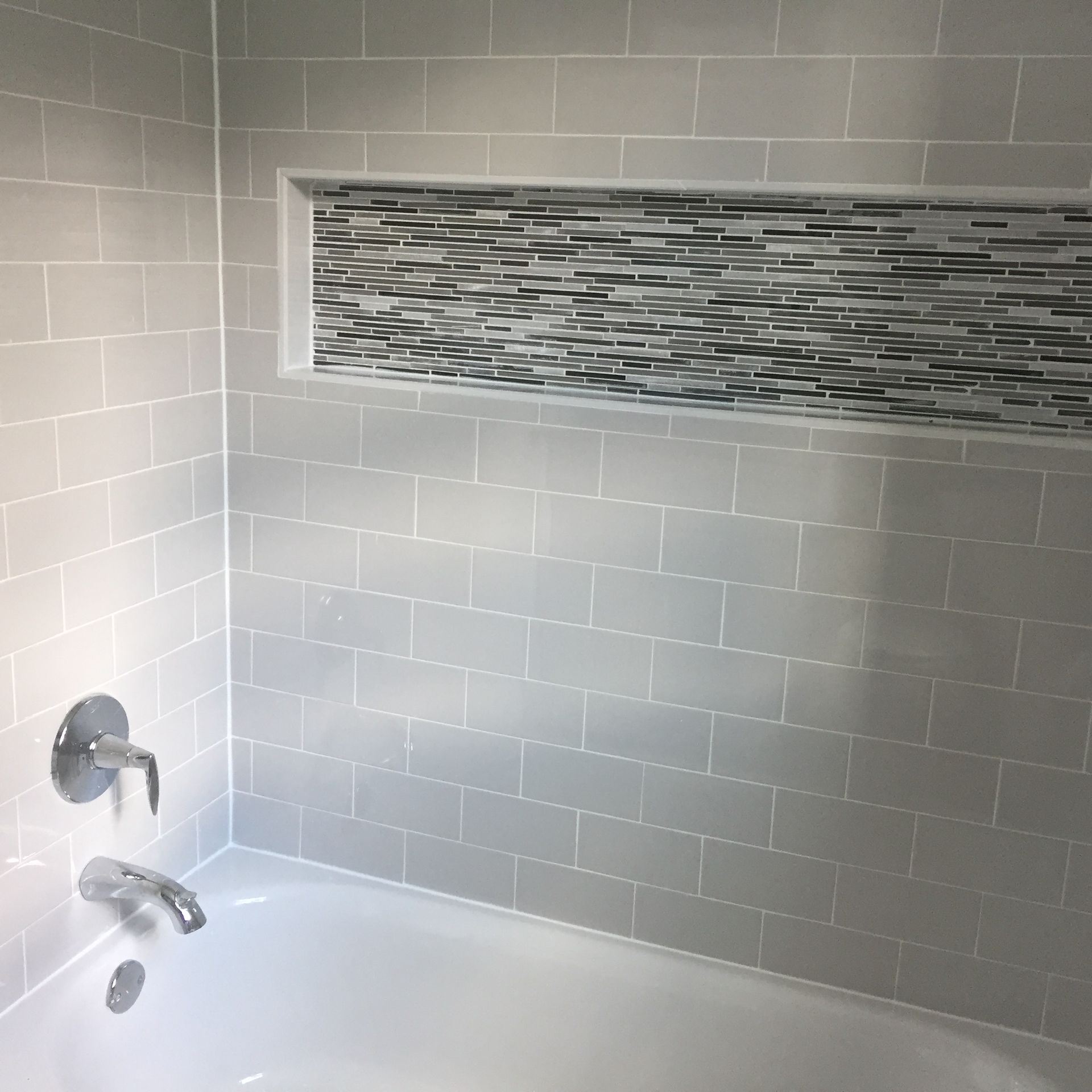 A bathtub in a bathroom with white brick walls and a mosaic tile niche.