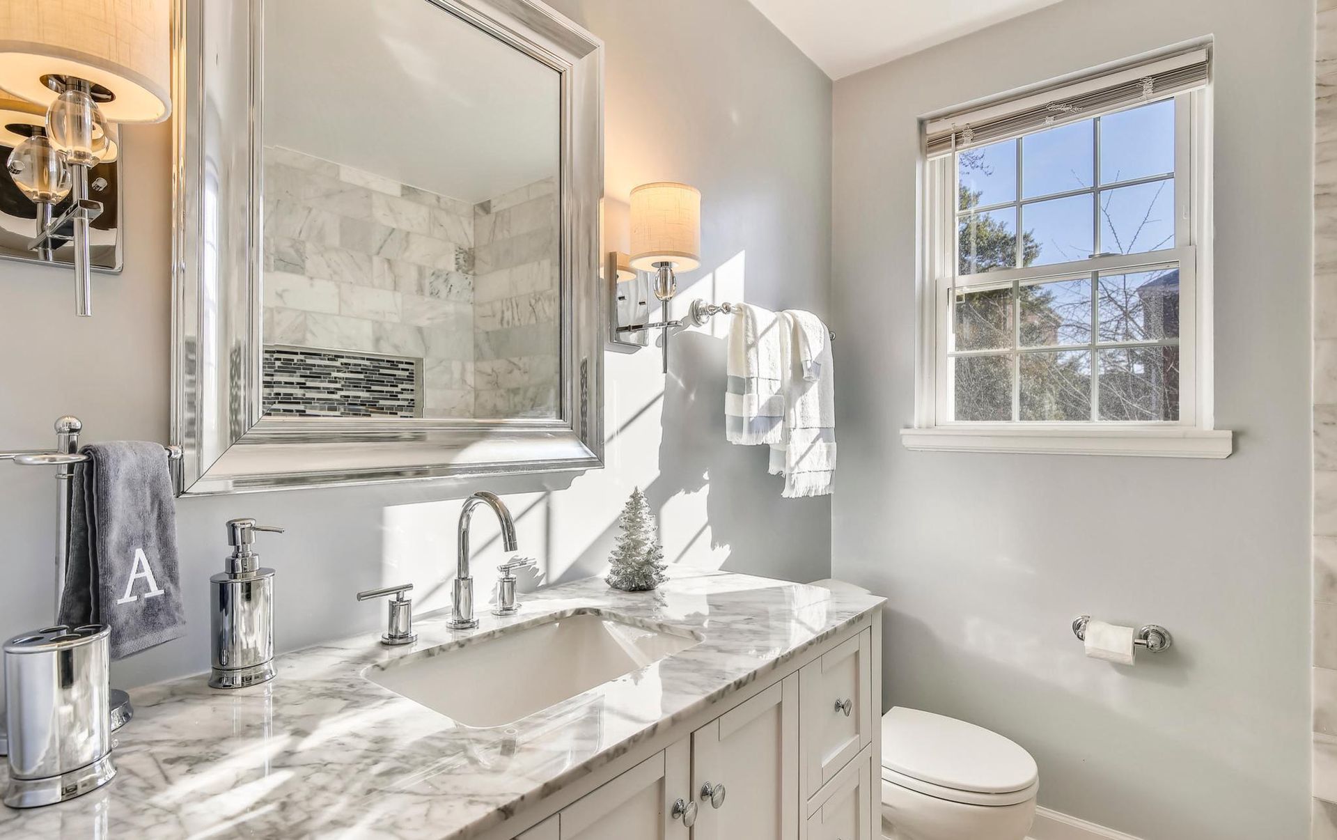 A bathroom with a sink , toilet , mirror and window.