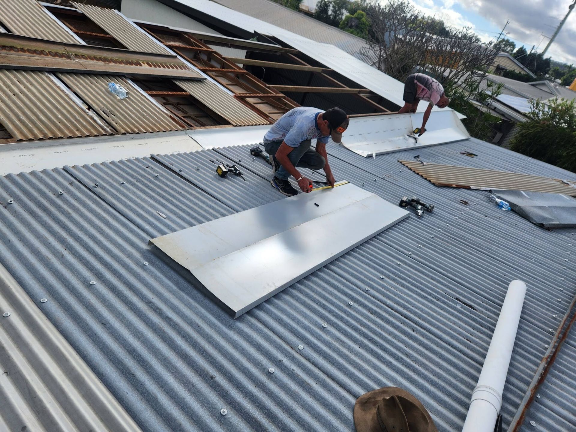 Workers Installing Metal Roofing Sheets on A Corrugated Rooftop — Sun Co Concrete And Construction in Tablelands, QLD