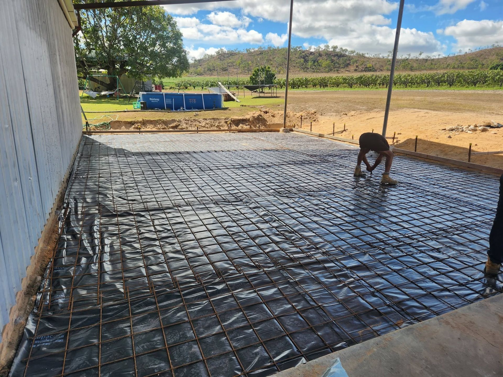 Worker Smoothing Wet Concrete Rebar Slab Beside a White Wall — Sun Co Concrete And Construction in Dimbulah, QLD