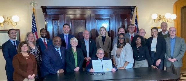 Group of advocates stand behind Governer Mike DeWine who holds up the signed legislation