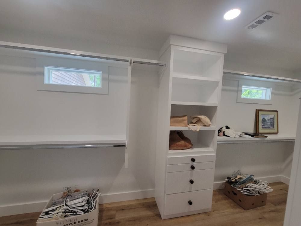 A walk-in closet with beige carpet, white built-in storage shelving, drawers, and a closed white door.