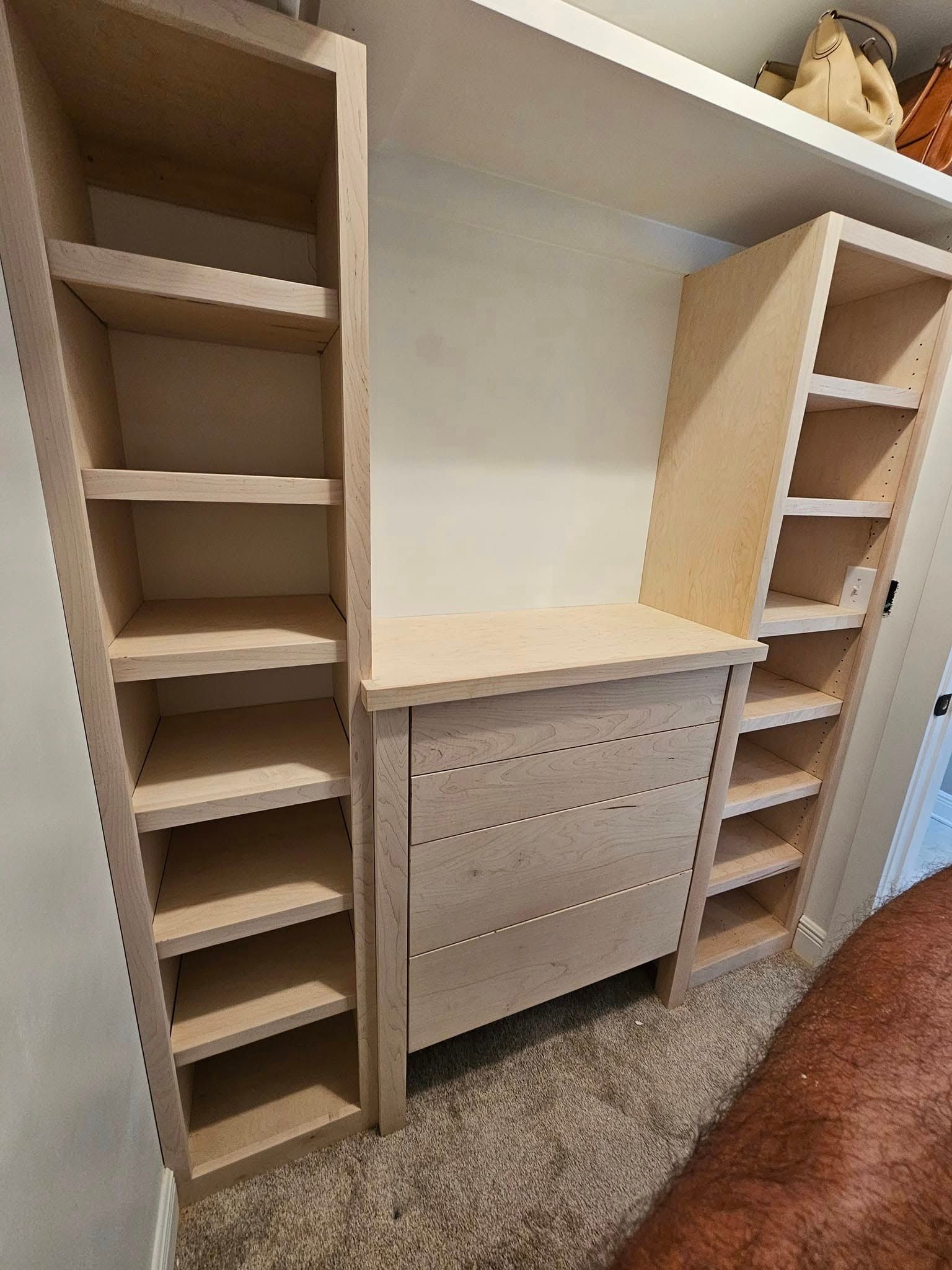 A walk-in closet featuring white modular shelving, hanging rods, and integrated drawers over dark hardwood floors.