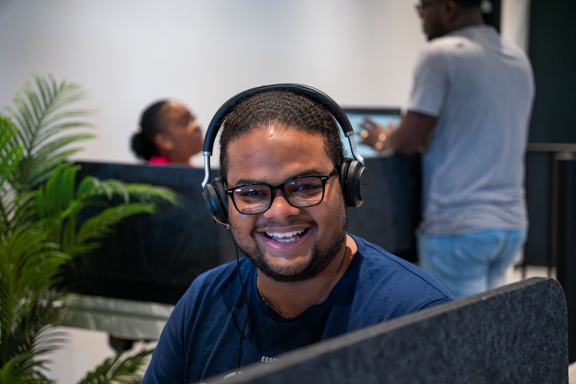 Een man met een koptelefoon op zit glimlachend achter een bureau voor een computer.