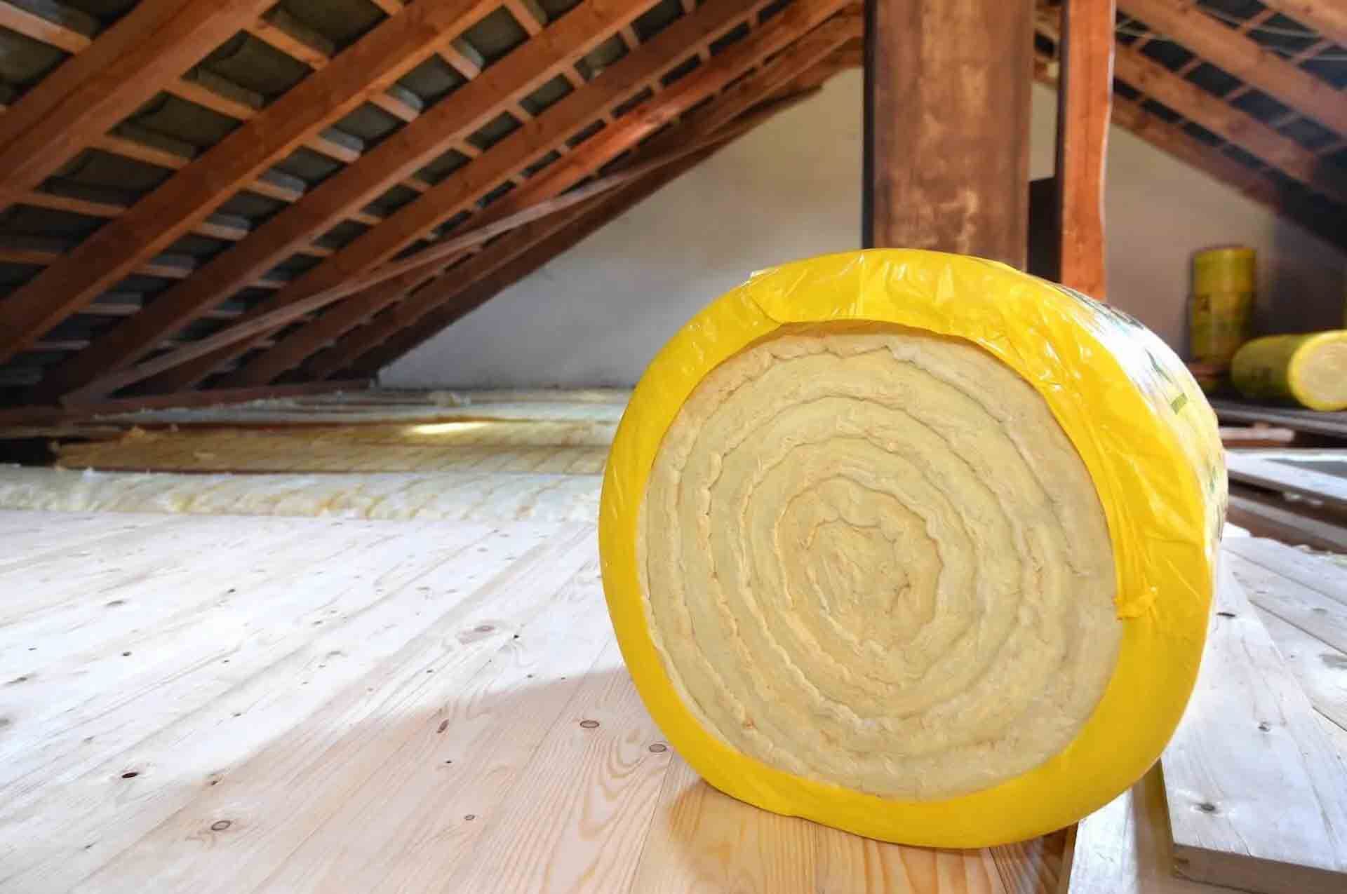 Roll of yellow insulation in an attic with exposed wooden rafters.