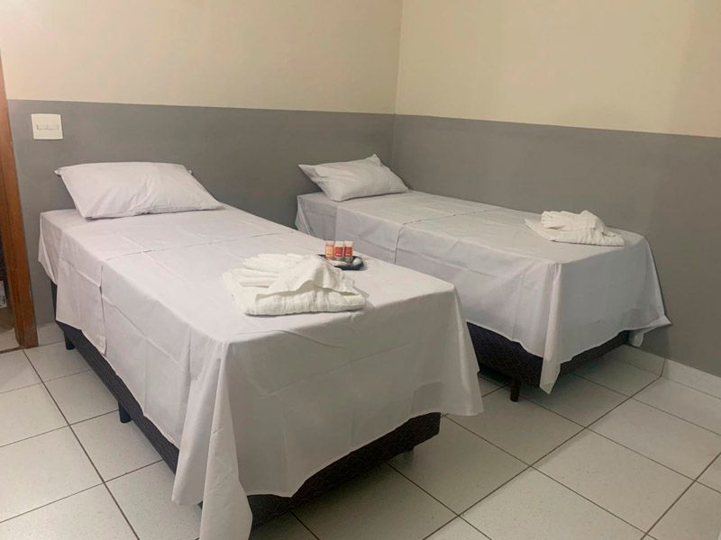 Um quarto de hotel minimalista com duas camas de solteiro, lençóis brancos, paredes cinza e piso de azulejo.