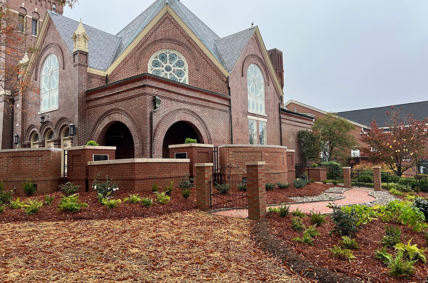 Brick church exterior with arched entry, stained glass windows, and autumn landscaping.