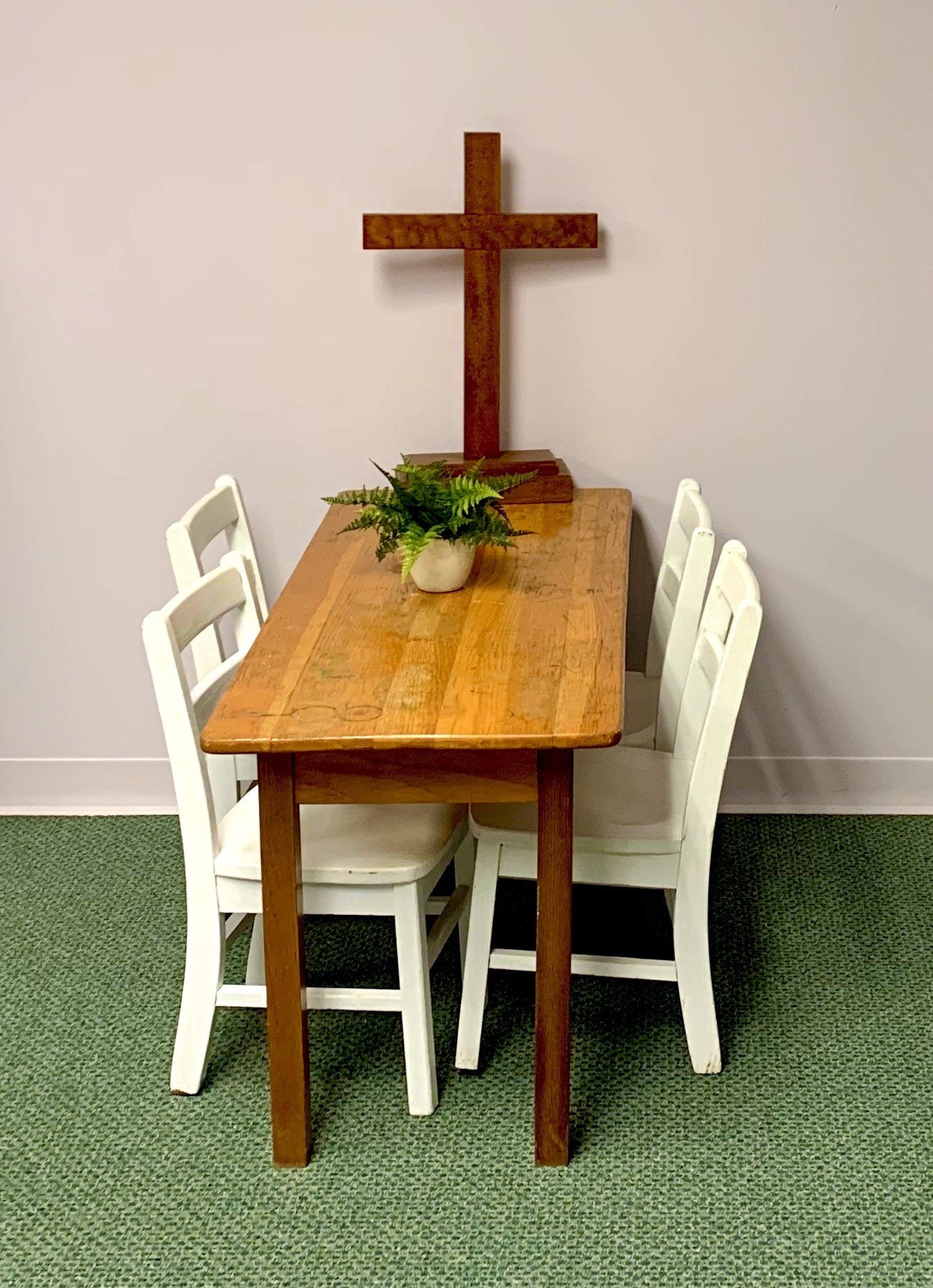 Wooden table and chairs in front of a cross; greenery on the table.