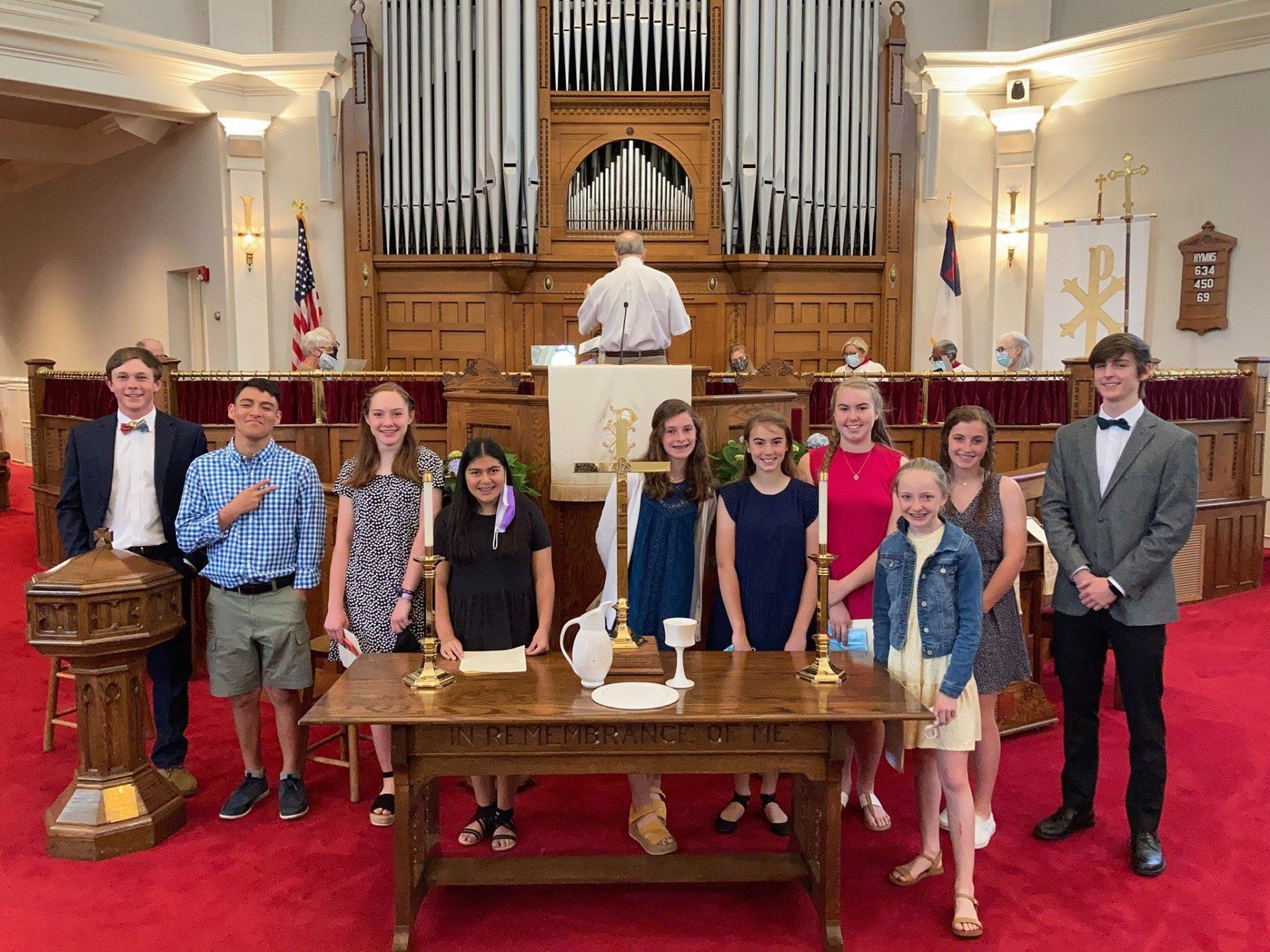 Group of youth at the front of the Sanctuary behind the communion table. Red carpet, organ backdrop.