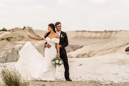 Bride and groom posing in a white desert landscape, bride’s dress flowing in the wind, bouquet in hand