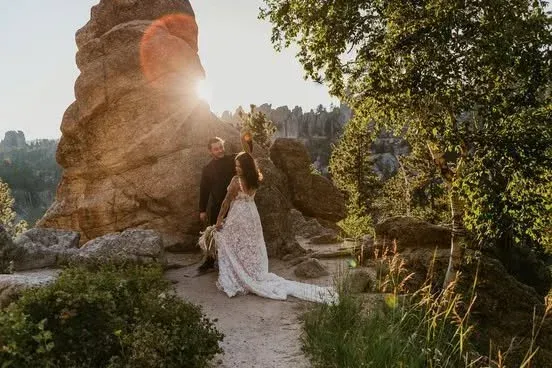 Bride and groom in a sunlit outdoor wedding scene beside a large rock formation