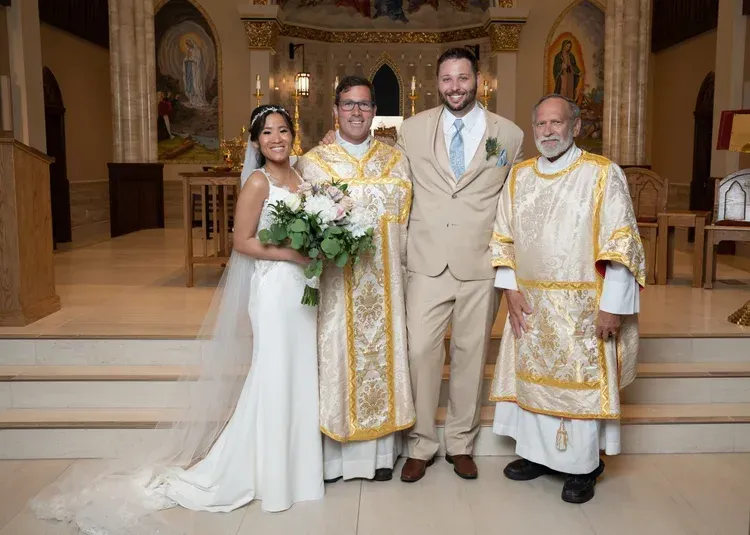Bride and three men posing at a church altar, two in gold vestments and one in a beige suit