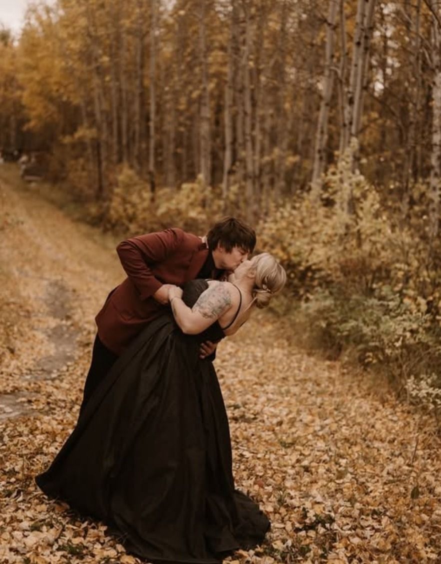 A couple embracing on a leaf-covered forest path in autumn.