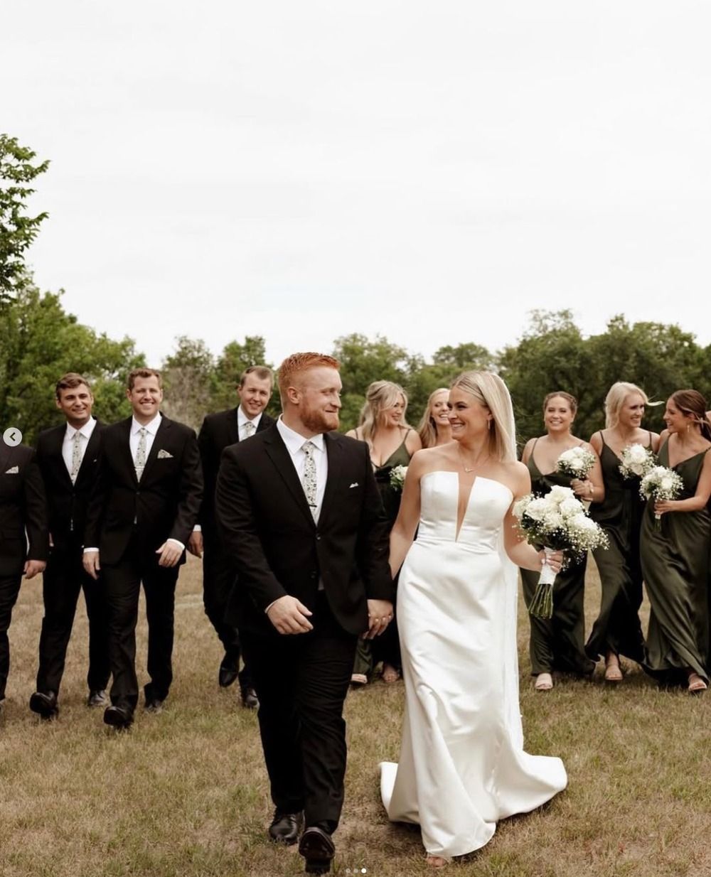 Wedding party walking outdoors, with the bride in a white dress and groom in a black tuxedo.