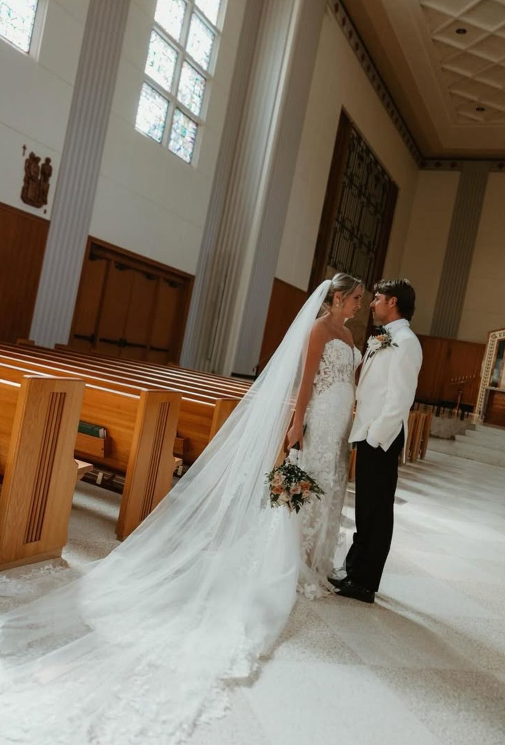 Bride and groom kissing in a church aisle, bride in long white veil and train