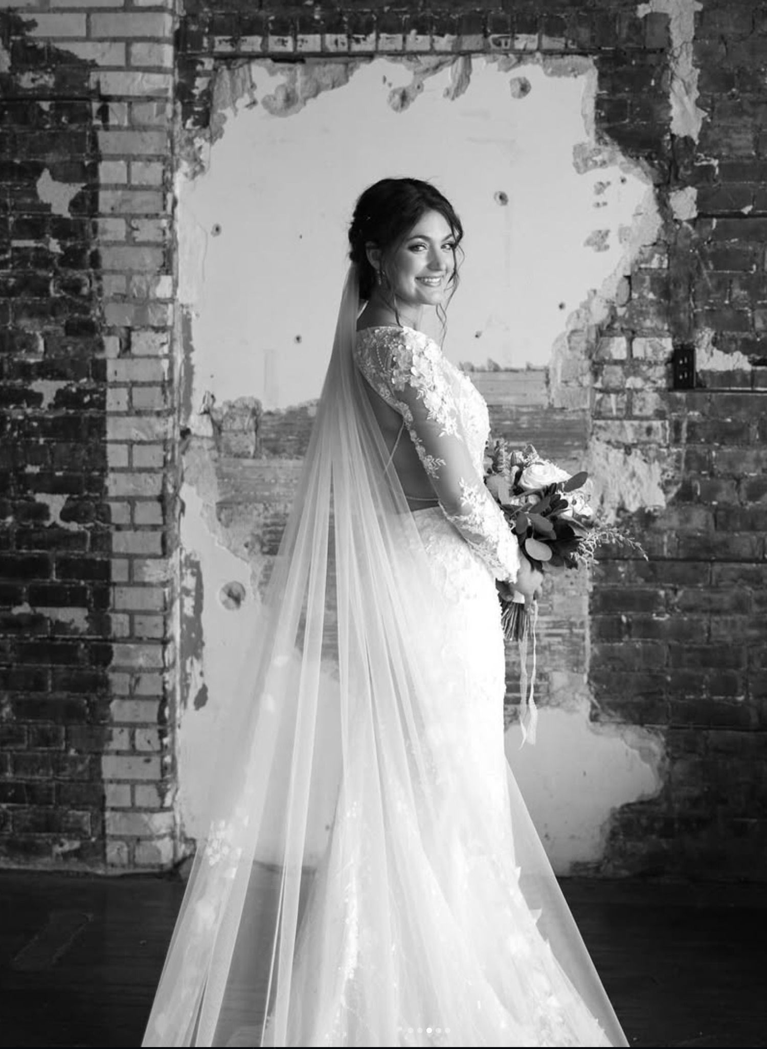 Woman in a flowing gown standing in a brick doorway, looking over her shoulder.