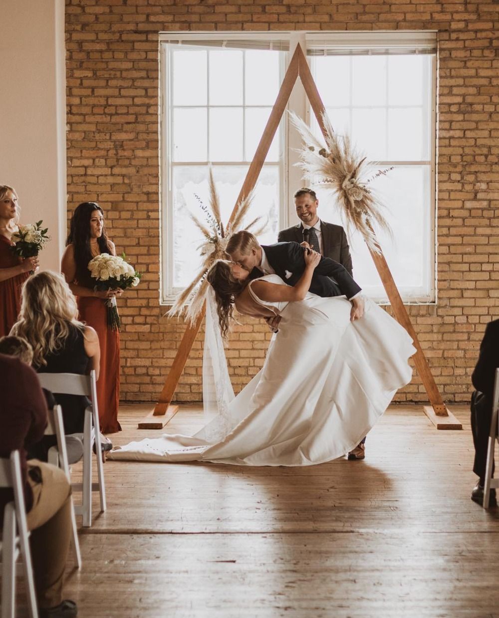 Wedding ceremony in a brick hall, with a couple dancing beneath a wooden arch and floral decor.