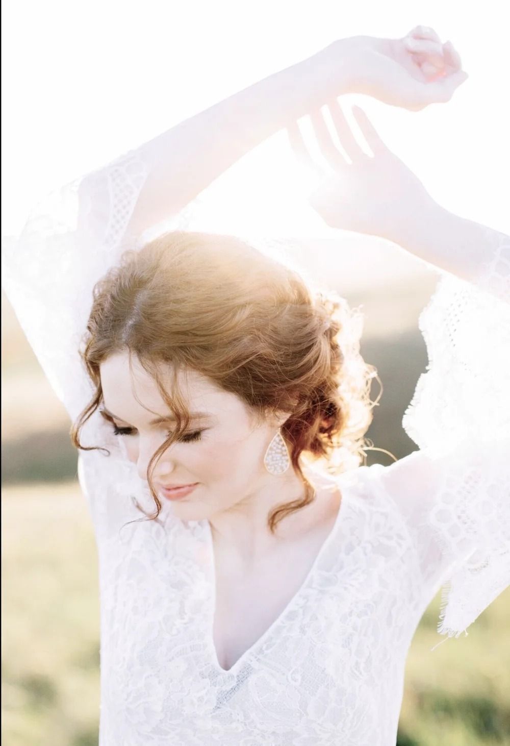 Woman in a white dress with arms raised in a sunlit outdoor field