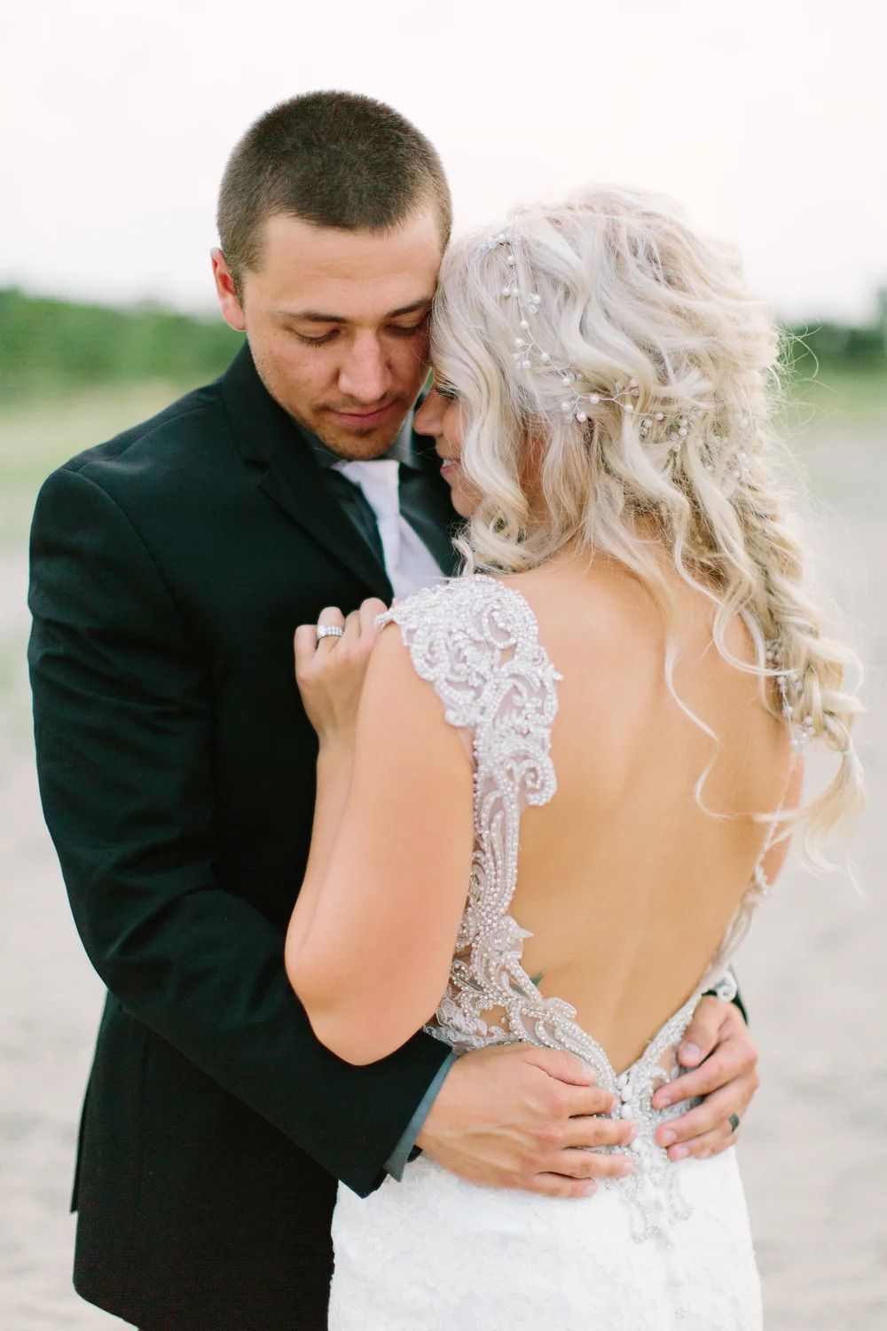 Bride and groom embracing outdoors, the bride in a white lace gown and the groom in a black suit