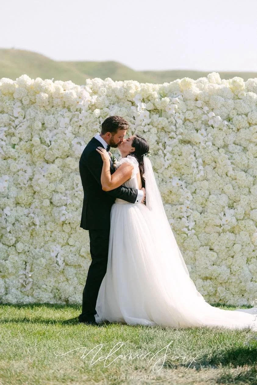 Bride and groom embracing outdoors in front of a white floral wall