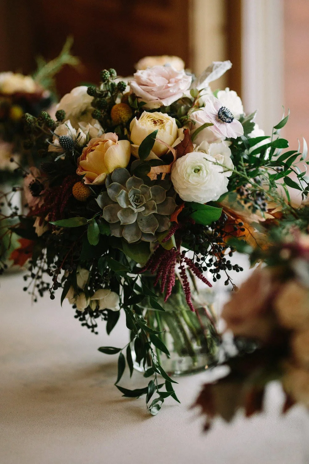 Hand-tied bouquet of cream, blush, and green flowers with cascading greenery on a table