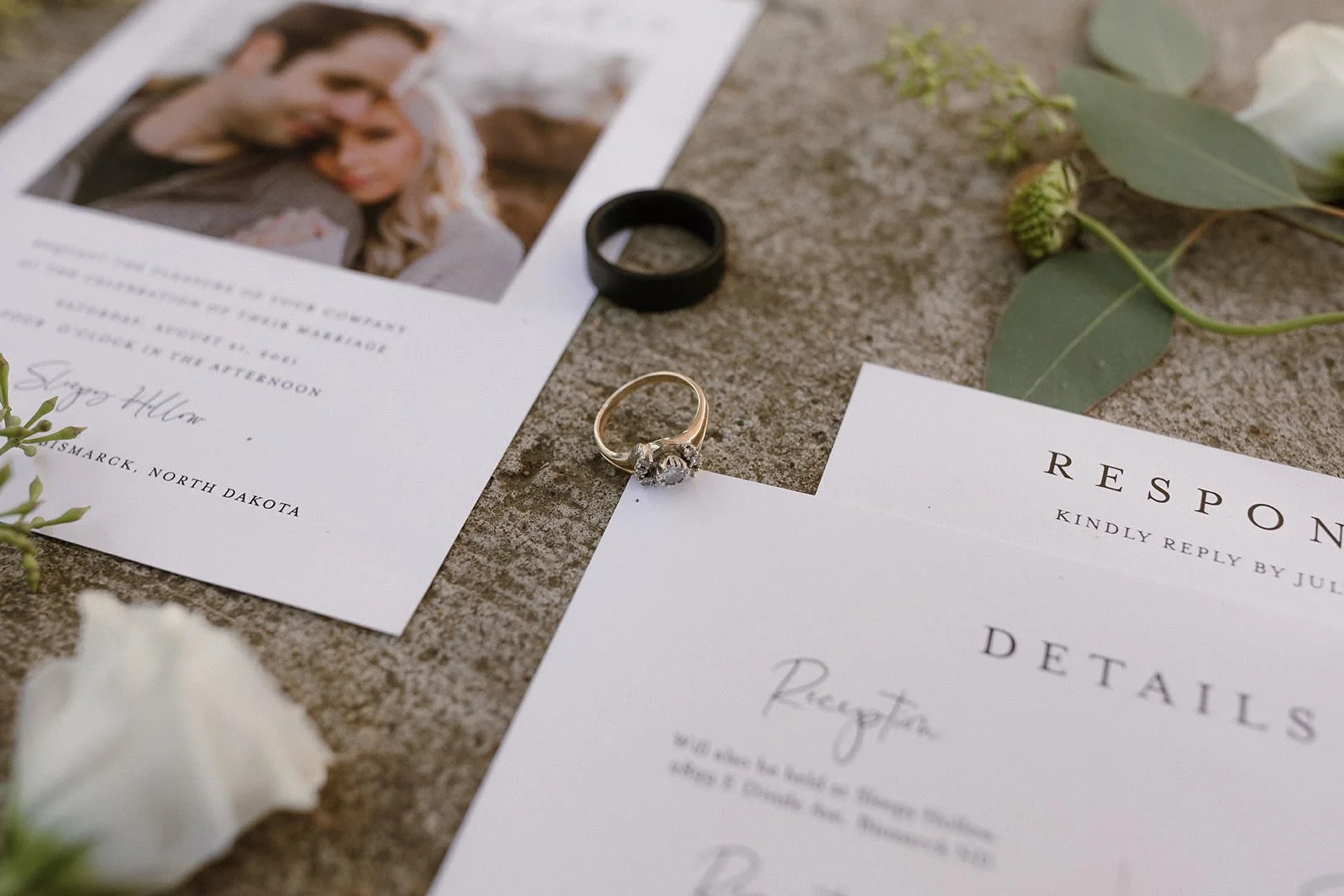 Wedding invitation suite with rings on a textured surface and a photo card nearby