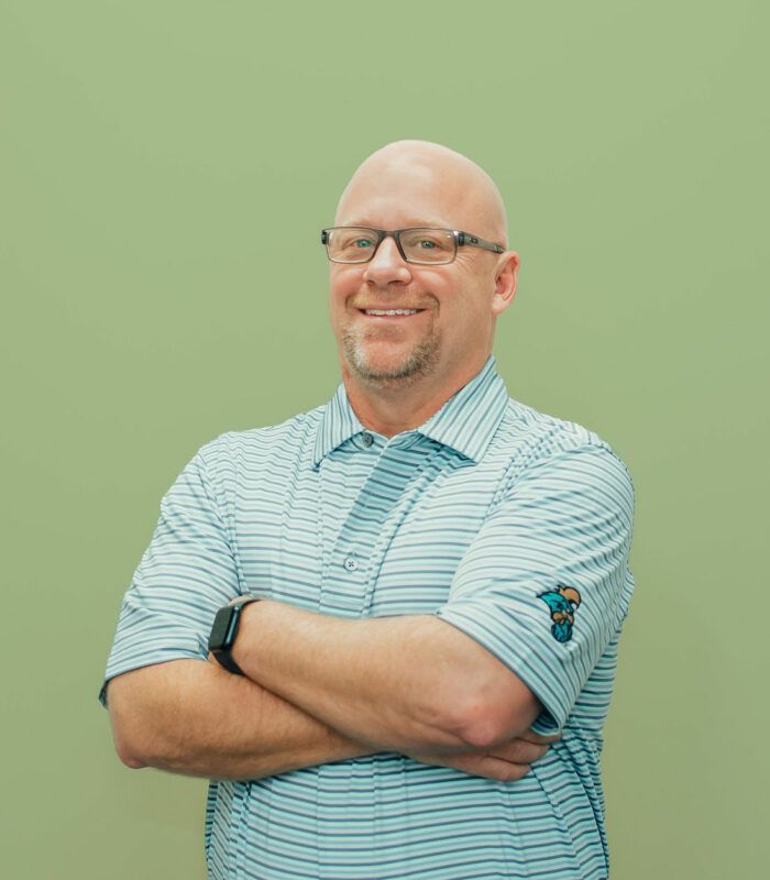 A man wearing glasses and a striped shirt is standing with his arms crossed.