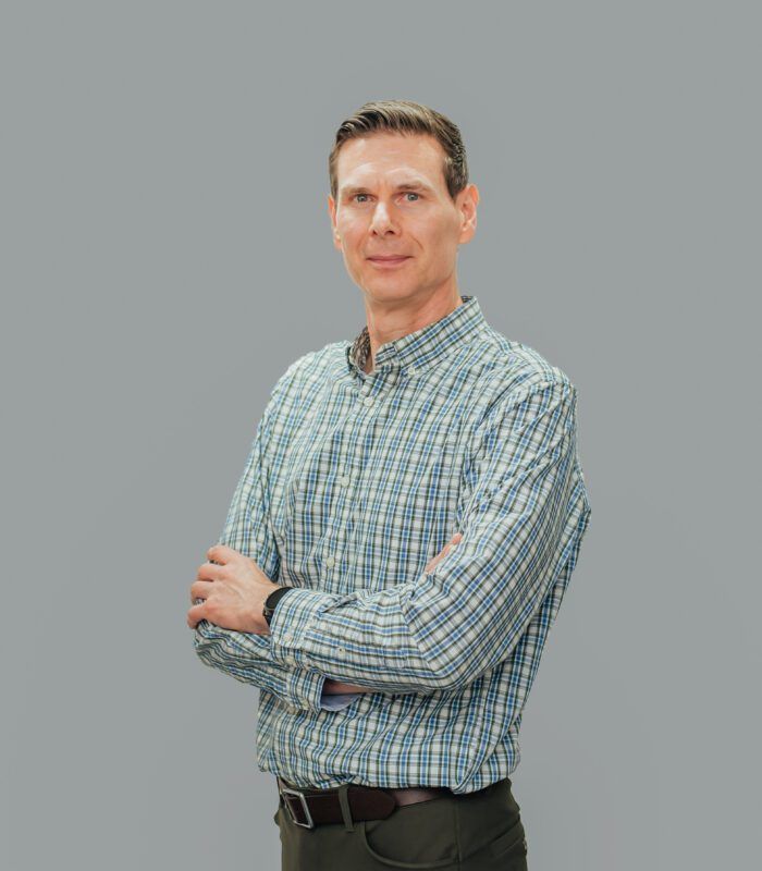 A man in a plaid shirt is standing with his arms crossed.