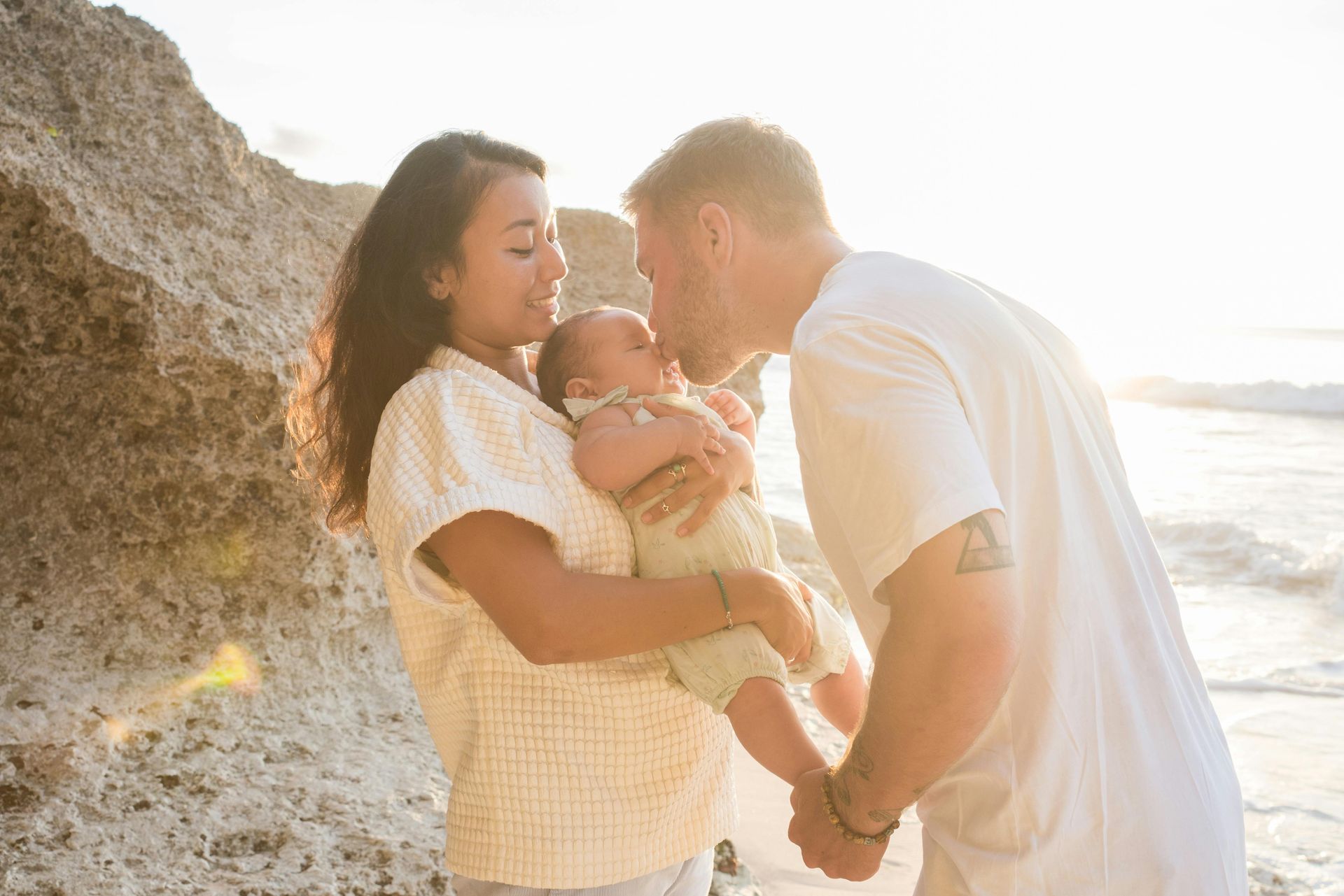 A man and a woman are holding a baby on the beach.
