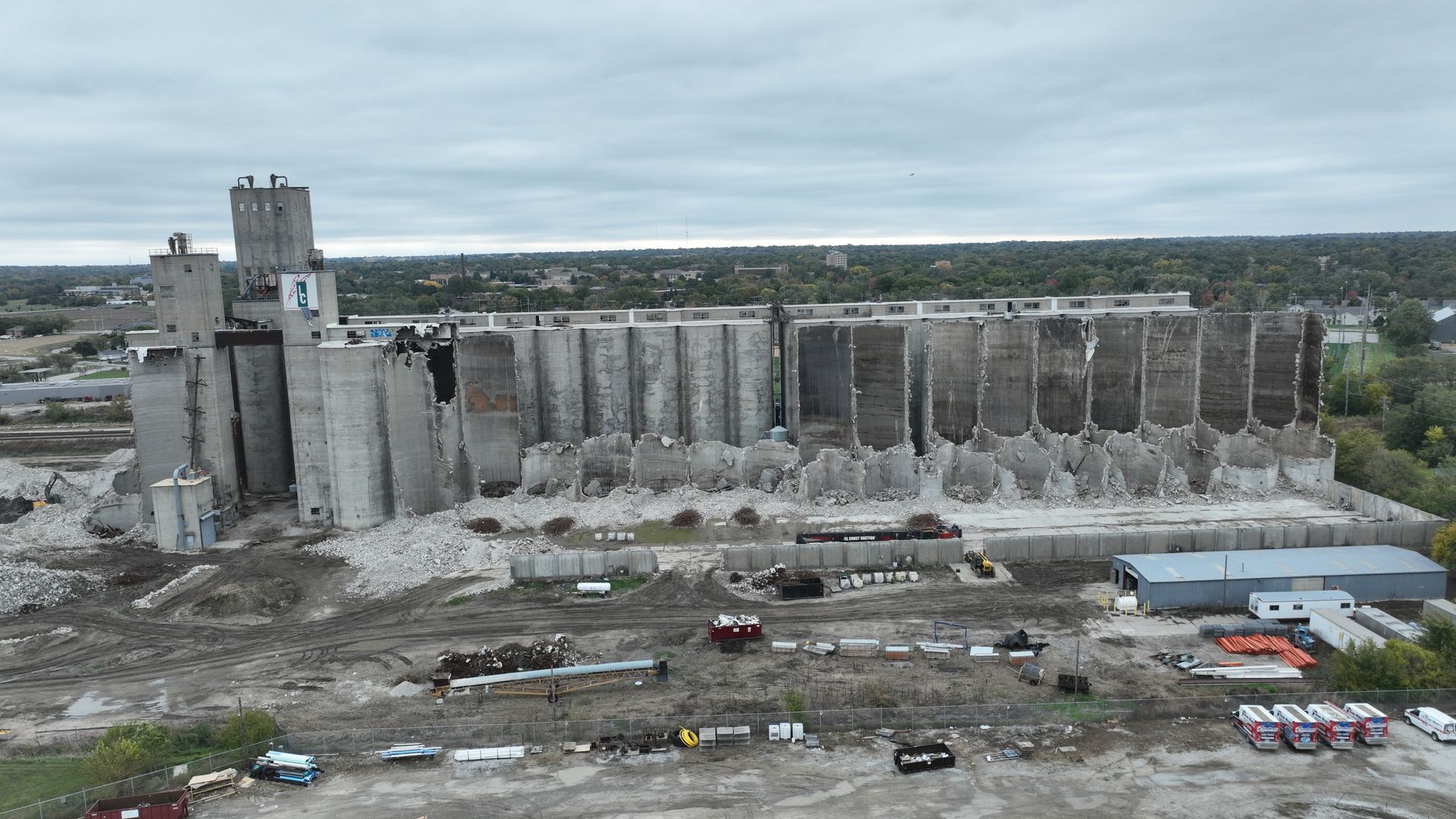 CL Construction demolition crew dismantling the historic Hansen-Mueller grain elevator complex at 3001 Cornhusker Highway in Lincoln, Nebraska. Heavy machinery, including a high-reach excavator with demolition claw, tears down sections of the massive concrete silos and storage structures on the 17.5-acre site south of Cornhusker Highway near 33rd Street, as part of a year-long project to clear the dilapidated landmark for future redevelopment