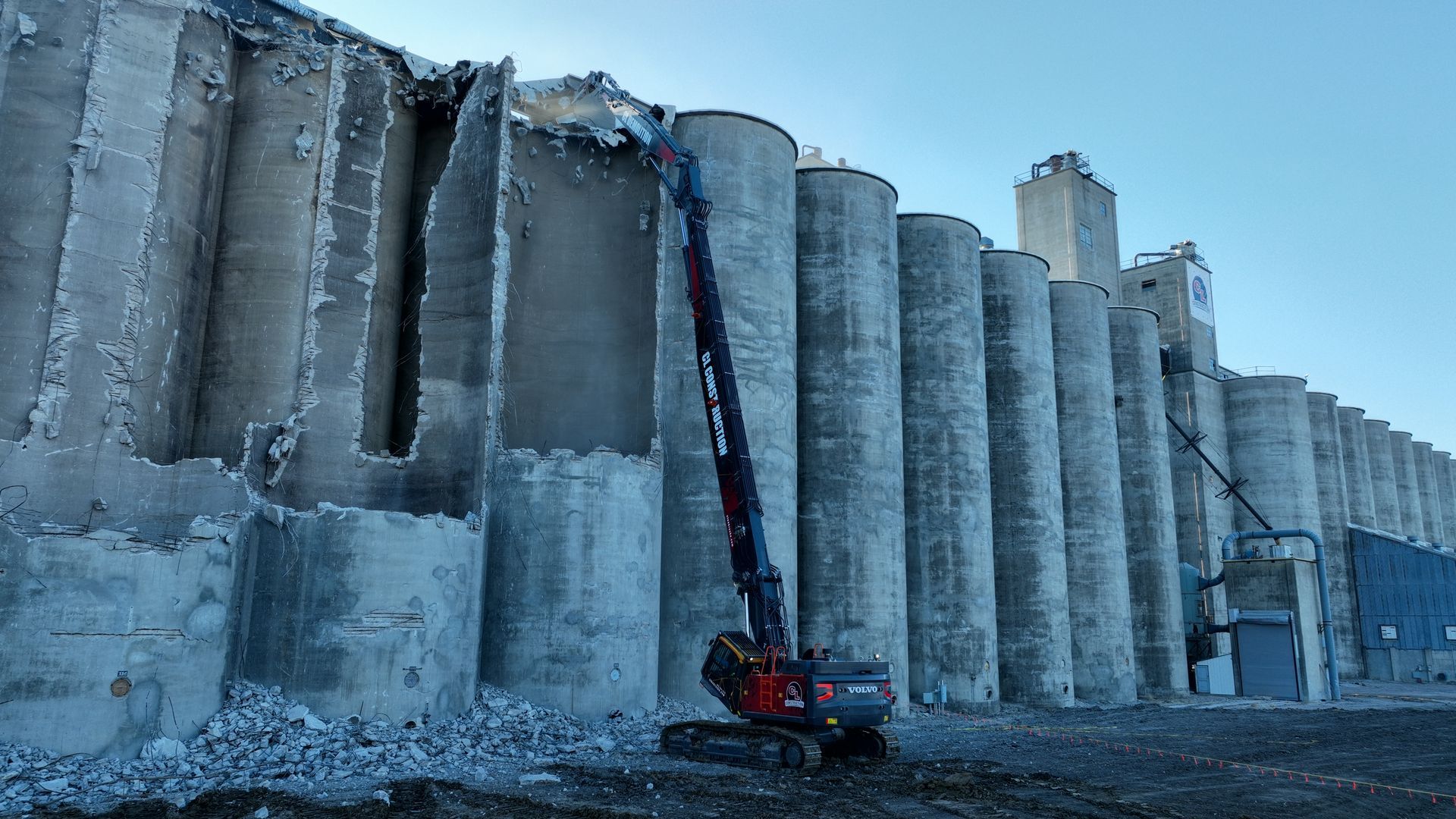 CL Construction demolition crew dismantling the historic Hansen-Mueller grain elevator complex at 3001 Cornhusker Highway in Lincoln, Nebraska. Heavy machinery, including a high-reach excavator with demolition claw, tears down sections of the massive concrete silos and storage structures on the 17.5-acre site south of Cornhusker Highway near 33rd Street, as part of a year-long project to clear the dilapidated landmark for future redevelopment